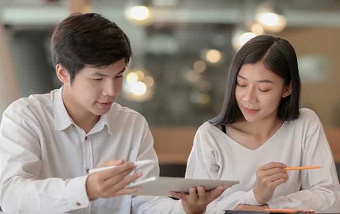 Instant-Loan-Approval - Oasis Credit Two colleagues review a tablet together as the man uses a stylus and the woman holds an orange pencil.